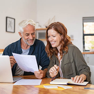 Mature smiling couple sitting and managing expenses at home. Happy senior man and mid woman paying bills and managing budget. Middle aged couple checking accountancy and bills while looking at receipt.