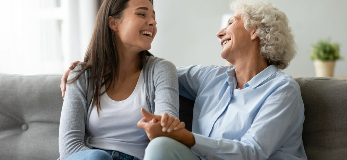 Happy,Elderly,Mother,And,Grown-up,Daughter,Sit,On,Couch,Laugh