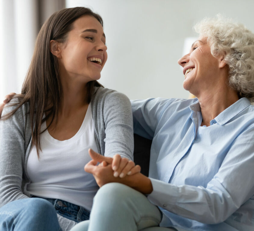 Happy,Elderly,Mother,And,Grown-up,Daughter,Sit,On,Couch,Laugh